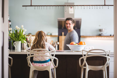 Father looking at daughter studying while sitting in kitchen