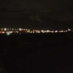 Defocused image of illuminated lights against sky at night