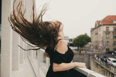 Young woman tossing hair while standing against building