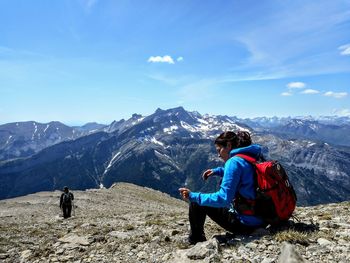 Side view of female hiker sitting on mountain against blue sky