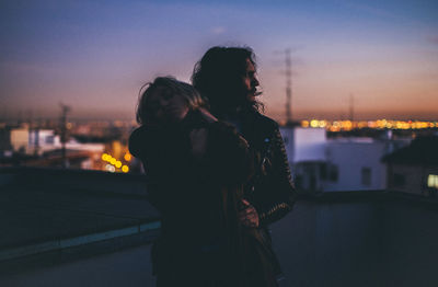 Silhouette woman standing by cityscape against sky during sunset