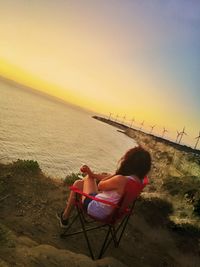 Woman sitting on beach against clear sky during sunset