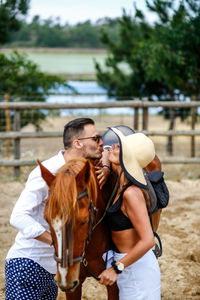 Side view of couple romancing while standing with horse on field