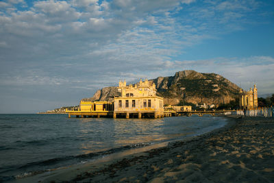 The old built structure on the water on beach by sea against sky.