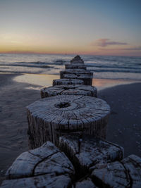 Stack of wooden posts on beach against sky during sunset