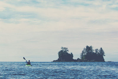 Rear view of man kayaking in sea against sky