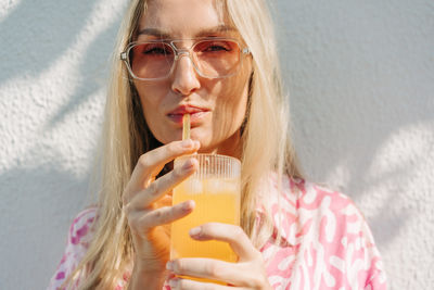 Portrait of young woman drinking water against wall