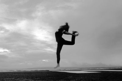 Full length side view of woman jumping at beach against sky