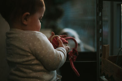 Side view of baby girl holding rope while sitting outdoors