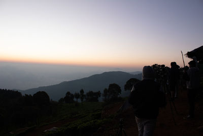 Rear view of people photographing mountains against sky during sunset