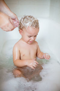 Cropped image of woman giving bath to boy sitting in bathtub