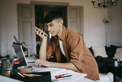 Young male freelancer talking on speaker phone while working on laptop at home office