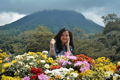 Portrait of smiling woman by flowering plant against mountain range