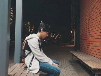 Side view of young man sitting in city at night