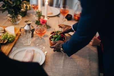 Midsection of man serving food to friend at dinning table in dinner party