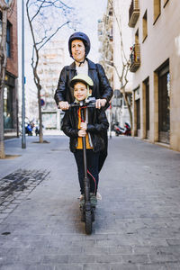 Mother and son riding electric scooter on footpath in city