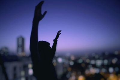 Silhouette man with arms raised against illuminated city at night