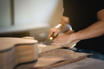 Midsection of craft person carving guitar at workshop