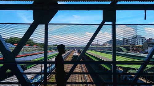 Silhouette of man standing against fence at railroad station