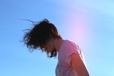 Low angle view of teenage girl standing against clear blue sky