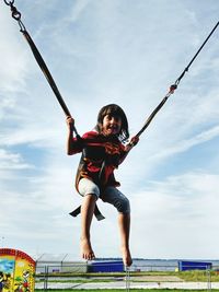 Full length portrait of happy girl jumping on swing against sky