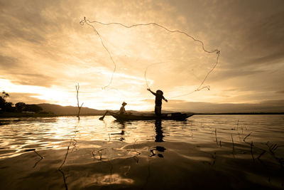 Man casting fishing net in lake against sky during sunset