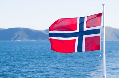 Norwegian flag waving by sea against sky