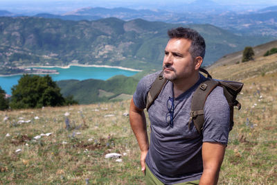 Man looking away while standing on grass against mountains