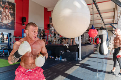 Determined male boxer in boxing gloves punching heavy bag during intense workout in gym