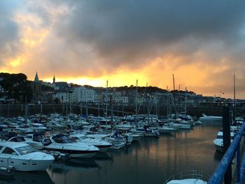 Boats moored at harbor against cloudy sky