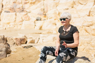 Old woman in black clothes sitting on a rock near the sea