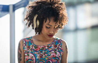 Fashionable young woman with curly hair listening music in city