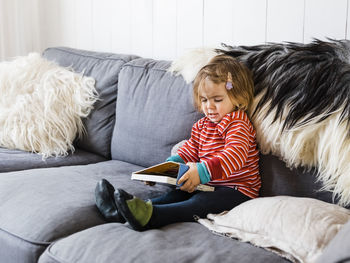 Girl holding book while sitting on sofa at home