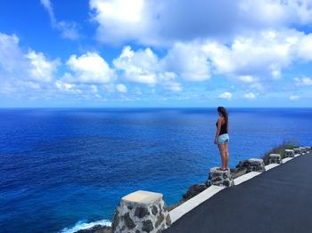 Woman overlooking calm blue sea against the sky