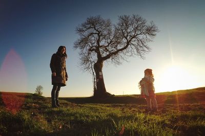 Mother looking at daughter holding doll on field against sky