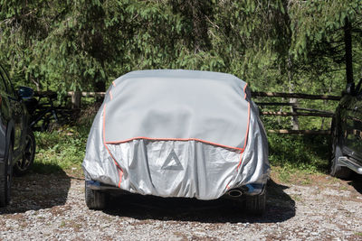 The gray and silver sun protection car cover. car parked in the forest parking  covered with a cover