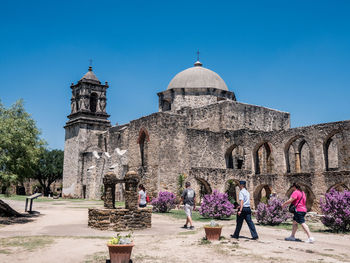 People walking in front of historical building against blue sky