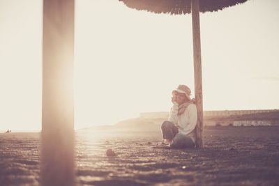 Woman sitting at beach against sky during sunset