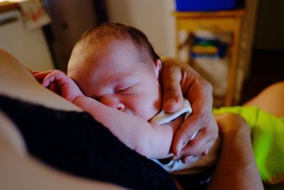  newborn baby sleeping on his mother chest while she is holding him with her hands 