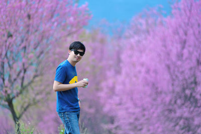 Portrait of man having drink while standing against pink flowering trees