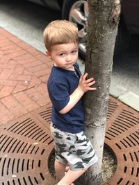 Cute boy standing by tree trunk in city