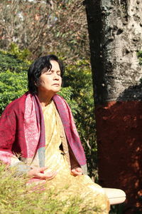 Senior woman meditating by tree trunk at park