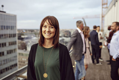 Portrait of smiling businesswoman with colleagues in background standing on terrace during party