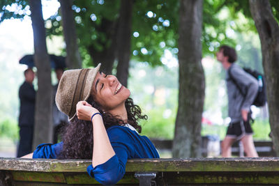 Woman sitting on bench against tree trunk