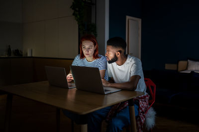 Young interracial couple looking at laptop discussing online family business, working late at home