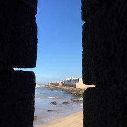 Buildings by sea against clear blue sky