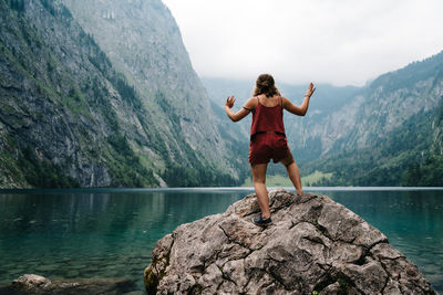 Rear view of young woman jumping on rock by lake