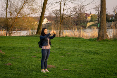 Full length of young woman standing on grassy field during sunset