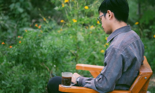 Side view of young man with tea sitting on bench