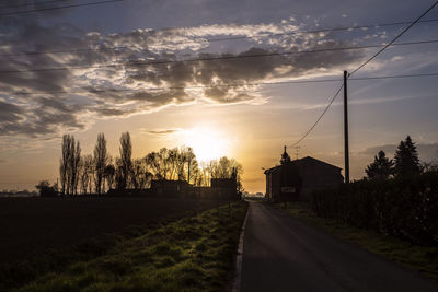 Road amidst trees and buildings against sky during sunset